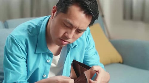 Nahaufnahme eines asiatischen Mannes mit einem Laptop, der Geld auf der Brieftasche überprüft, bevor er den Kopf schüttelt