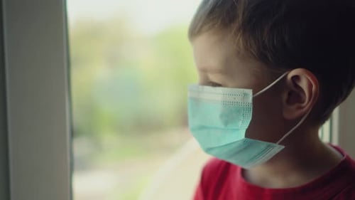 Child in Medical Mask Holds Toy by Window