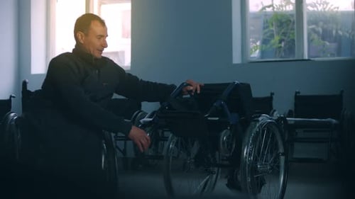 Side View of One American Male Workers in a Workshop at a Factory Making Wheelchairs Sitting at a