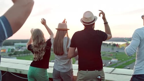 Rear View Group of People Enjoying Beautiful City Landscape Raising Arms on Rooftop Party at Sunset
