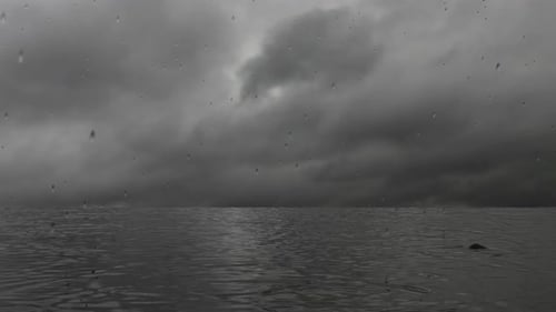 Rain on the lake, gray storm clouds. Rain intensifies on a sea of water with reflections