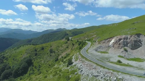 Car Driving Along the Empty Gravel Road Through Green Meadows Landscape on Sunny and Warm Day