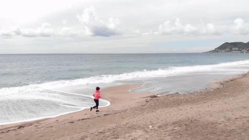 Woman Runs on Sandy Beach by Ocean