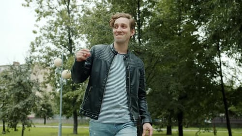 Slow Motion of Cheerful and Friendly Man Walking Outdoors in City Park Waving Hand and Dancing