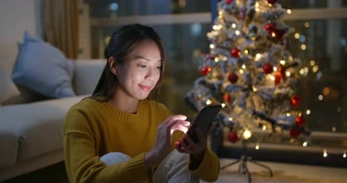 Young Woman Using Phone by Christmas Tree at Night