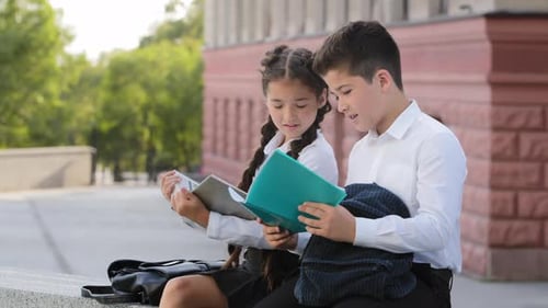 Zwei hispanische Kinder, Schüler, die nach dem Unterricht im Freien sitzen und Bücher lesen