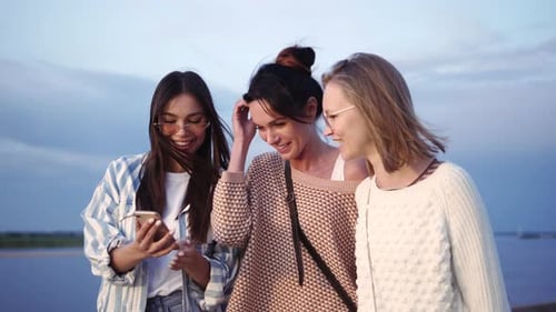 Three Friends Laughing Together at Smartphone by River