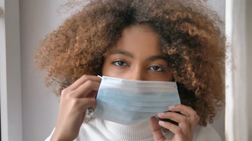 Portrait of a Young African American Girl Putting on a Medical Mask, Looking at the Camera