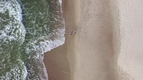 VISTA AÉREA: Vista superior de una pareja joven caminando cerca de la orilla del mar en un día nublado