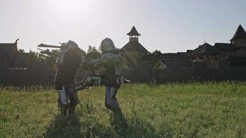 Battle of Two Knights in Armor Near Wooden Fortress. Knights Are Fighting Against Blue Sky with Sun.