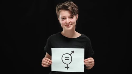 Smiling Beautiful Caucasian Young Woman Posing at Black Background Holding Sign of Gender Equality