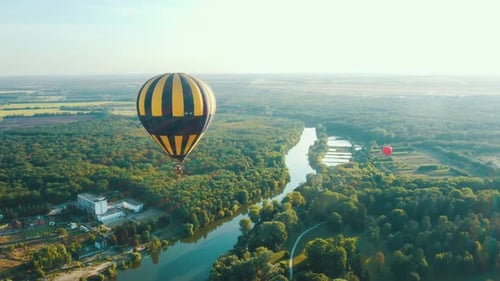 Aerial View of a Hot Air Balloon Flies Over the Trees Along the River. Fantastic Summer Sunset Scene