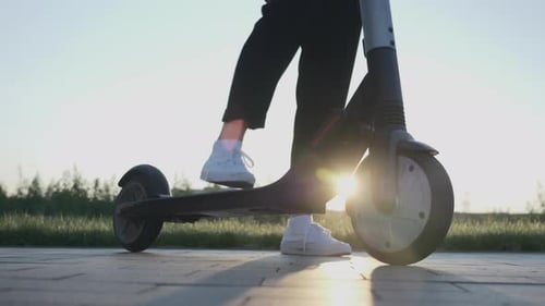 Female starting to ride on electric scooter in city at sunset. Alternative transportation concept