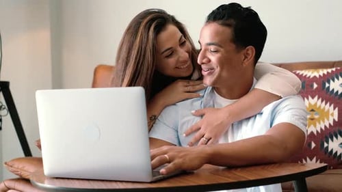 Close up of young couple working on laptop at home - happy people enjoy online computer