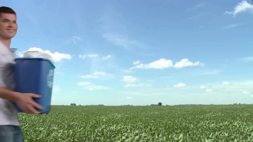 Man in field holding recycling bin with plastic bottles