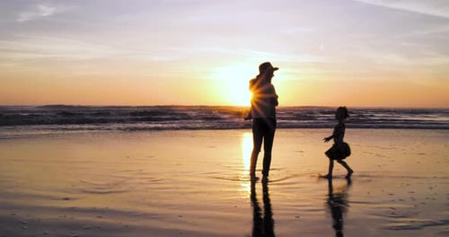A mother enjoys sunset at the beach with her two children as her daughter runs up to ask if they can