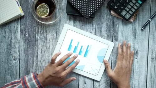 Man's Hand Working on Digital Tablet at Office Desk Using Self Created Chart