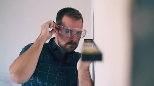 Un homme aux lunettes utilise un niveau moderne pour vérifier le mur d'une pièce