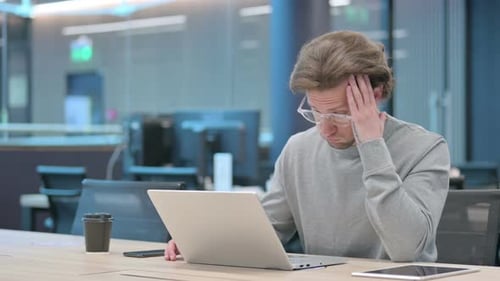 Tired Man Working on Laptop in Modern Office