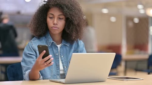 Young Adult Using Phone at Desk with Laptop