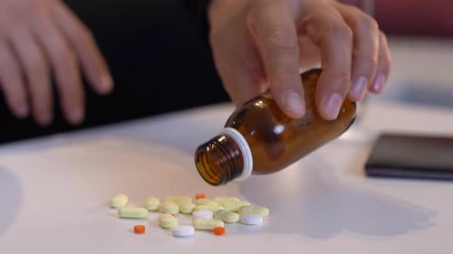 Hand Pouring Pills from Bottle onto Table