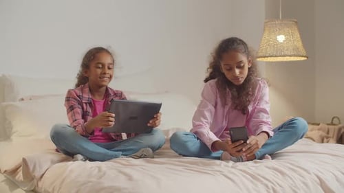 Girls Using Tablets and Smartphones on Bed