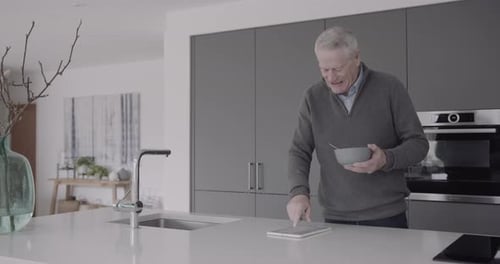 Senior Man Eats and Uses Tablet in Kitchen