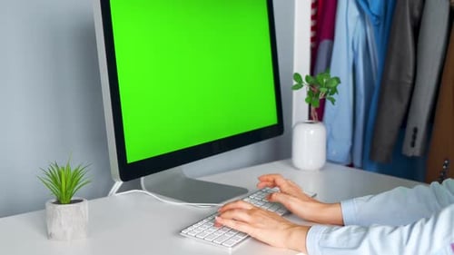 Woman Typing on a Computer Keyboard at Home Office, Monitor with a Green Screen. Chroma Key. Copy