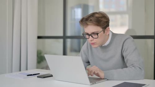 Young Man Celebrating Success While Using Laptop in Modern Office