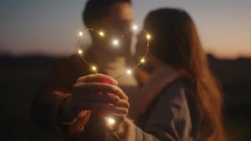 Couple Embraces with Heart Lights at Sunset