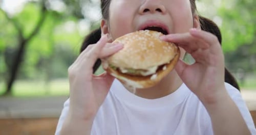 Girl Enjoys Eating a Hamburger in a Park