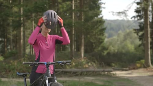 Woman Cyclist Puts on Helmet in Forest