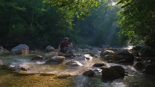 Männlicher Reisender genießt die Schönheit der Natur am Fluss im Wald bei Sonnenuntergang