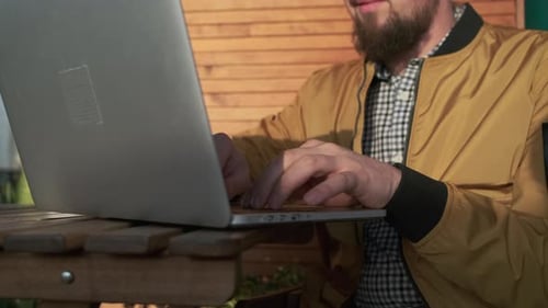 Man with Beard Typing on Laptop Outdoors