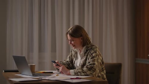 Woman Using Smartphone at Table with Laptop
