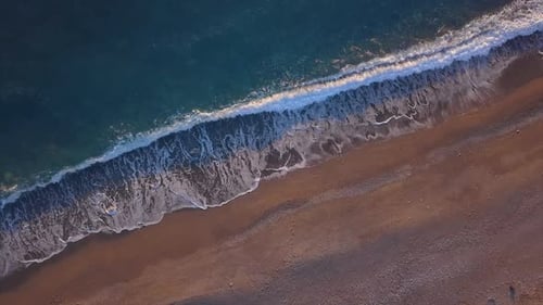 Top Down View Turquoise Waves Reaching Shore Break on Empty Pebble Beach. Golden Hour Sunset
