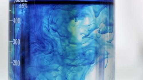 Close up view of blue liquid mixing around with clear liquid