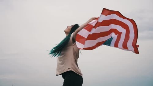 Young Woman Holding American Flag Against Cloudy Sky