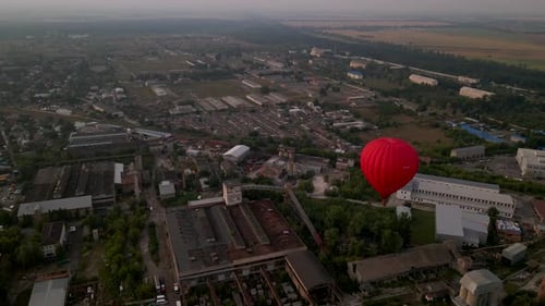 Red Hot Air Balloon Flying Over Buildings in Industrial Zone in Small European City at Summer Sunset