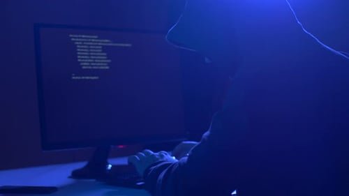 Hooded Hacker Typing Code on Computer at Night
