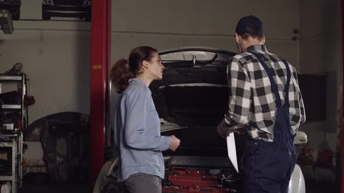 Cute Car or Automotive Technician Wearing Work Robe and a Cap Writes Down in His Notepad Complaints