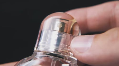 Man Takes Off Cap From Perfume Bottle on Dark Background