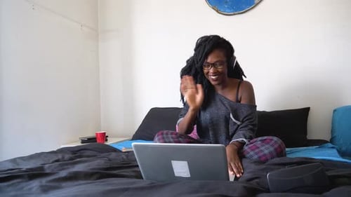 Junge Frau sitzt während eines Videoanrufs per Laptop auf dem Bett