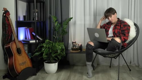 Woman Sitting with Laptop and Guitar in Home
