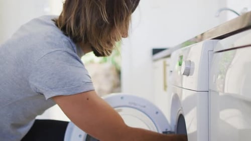 Man Loading Clothes Into Washing Machine At Home