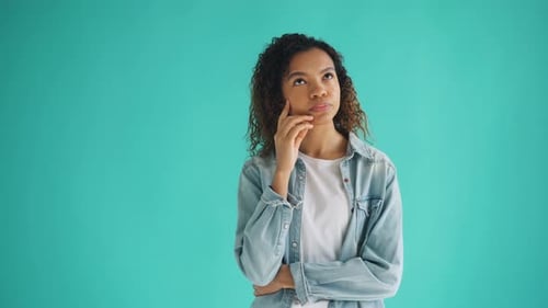 Portrait of Thoughtful Beautiful Girl Looking at Camera on Blue Background