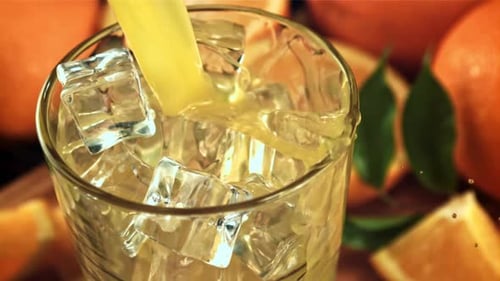 Orange Juice Pours Into Glass With Ice Cubes
