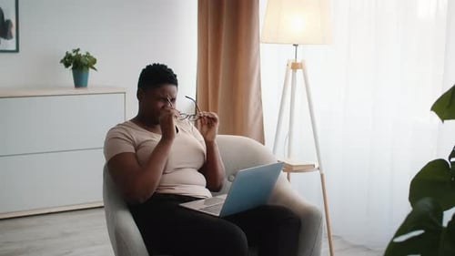 Afrikanische Frau nimmt mit Laptop die Brille ab und hat Augenschmerzen im Haus