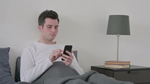 Young Adult Man Using Smartphone in Bed