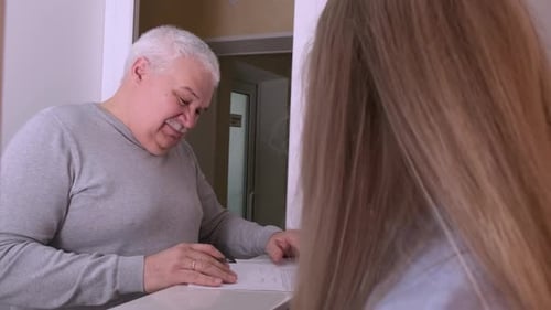 Elderly Client Signing Paper at Reception Desk In Medical Clinic